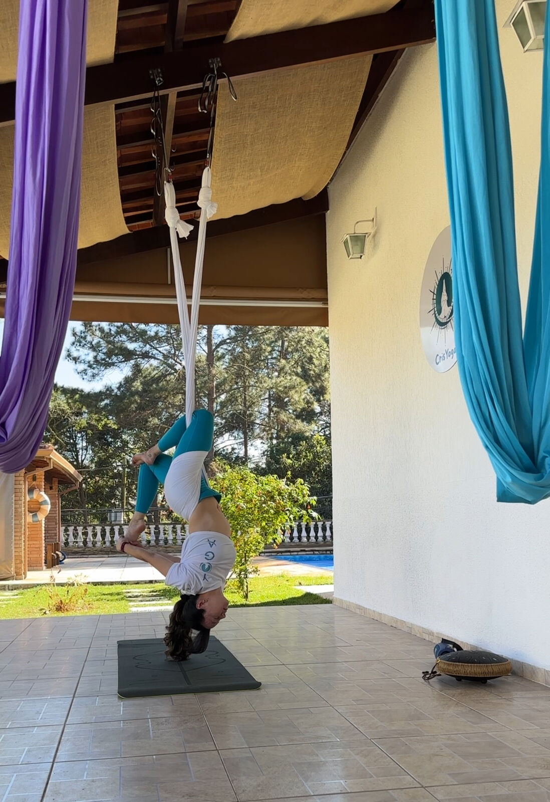 Cristína praticando Aerial Yoga no espaço coberto do studio, com vista para o jardim